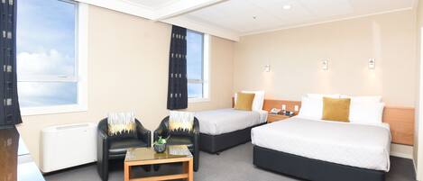 A hotel room with two beds, a desk, a chair, and a large window.