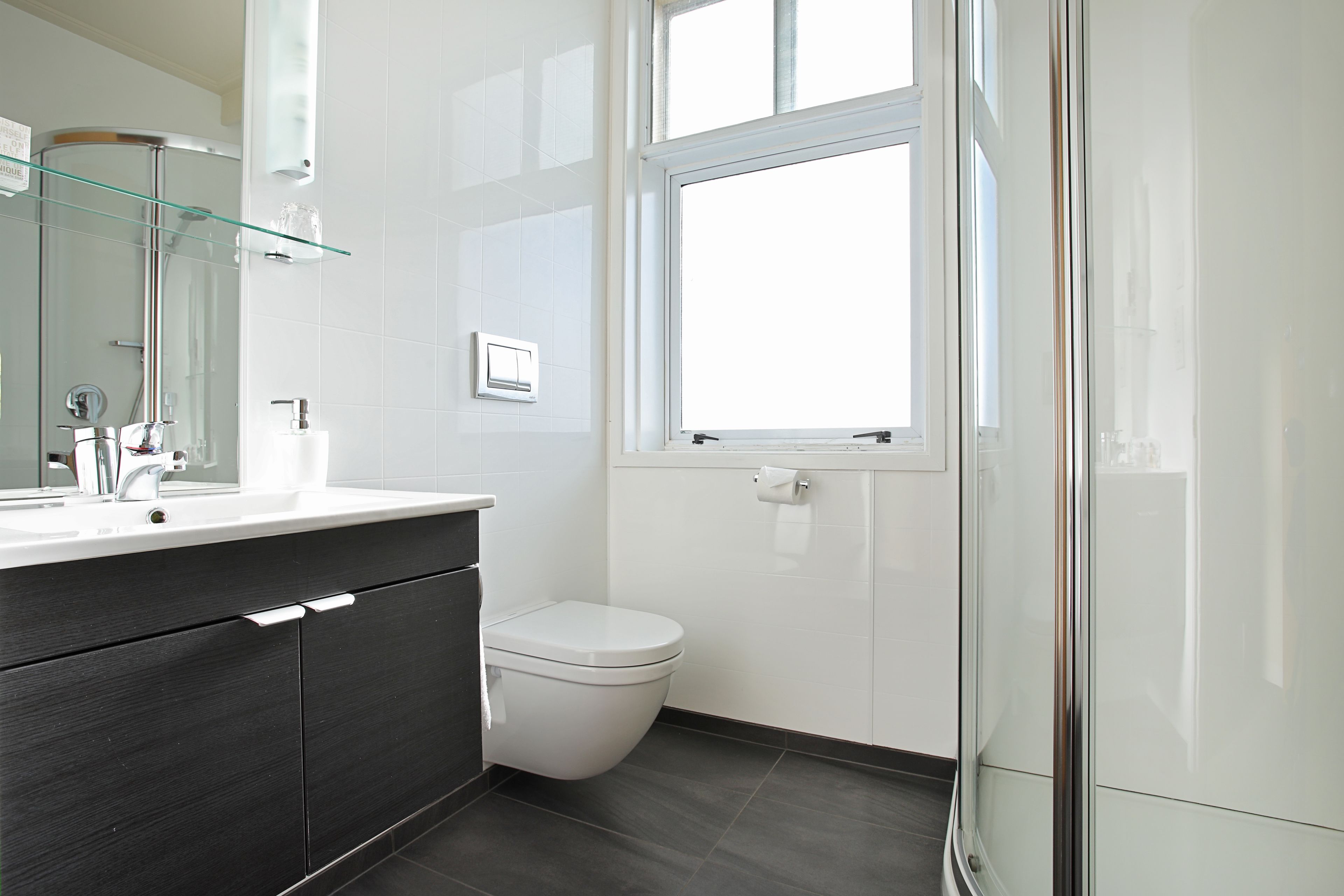 A modern bathroom with a glass shower enclosure, a white toilet, and a large window providing natural light.