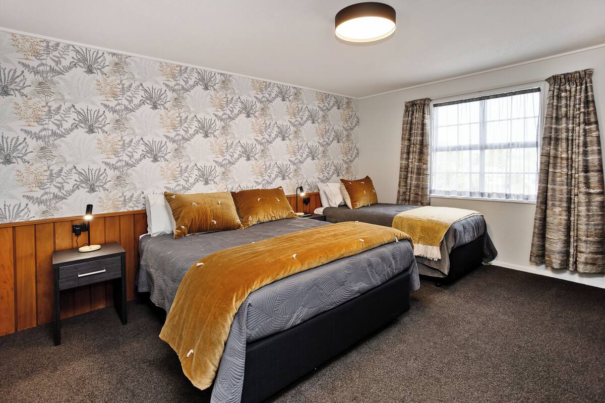 A bedroom with two beds, a nightstand, a lamp, and a window with curtains.