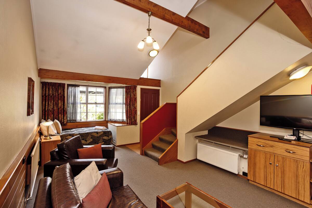A spacious living room with a sofa set, a television, and a staircase leading to an upper level.