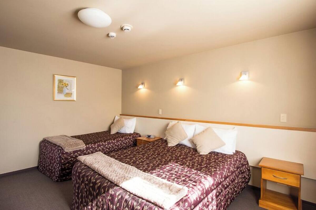 A hotel room with two beds, a small bedside table, a nightstand, and a wall-mounted light fixture.