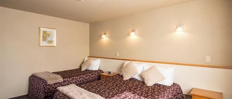Habitación de hotel con dos camas, una mesita de noche pequeña y una lámpara fijada a la pared.