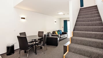A modern hotel room with a dining area, a sofa set, and a staircase.