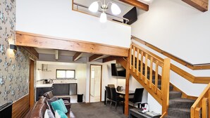 A spacious living area with a brown leather couch, a wooden staircase, and a kitchen in the background. - Balmoral Lodge Motel (Invercargill)