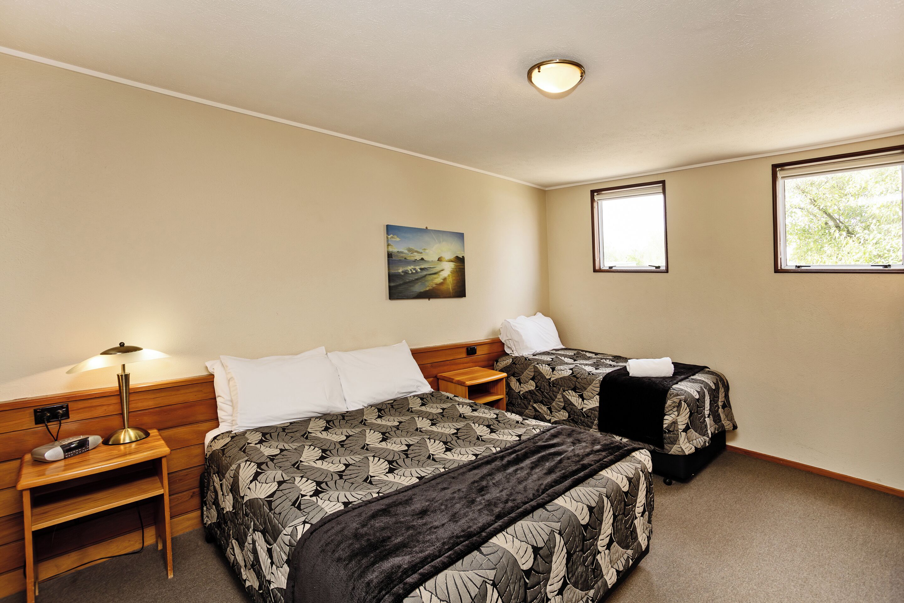 Quarto de hotel com duas camas, uma mesa de cabeceira, um abajur e um quadro na parede.