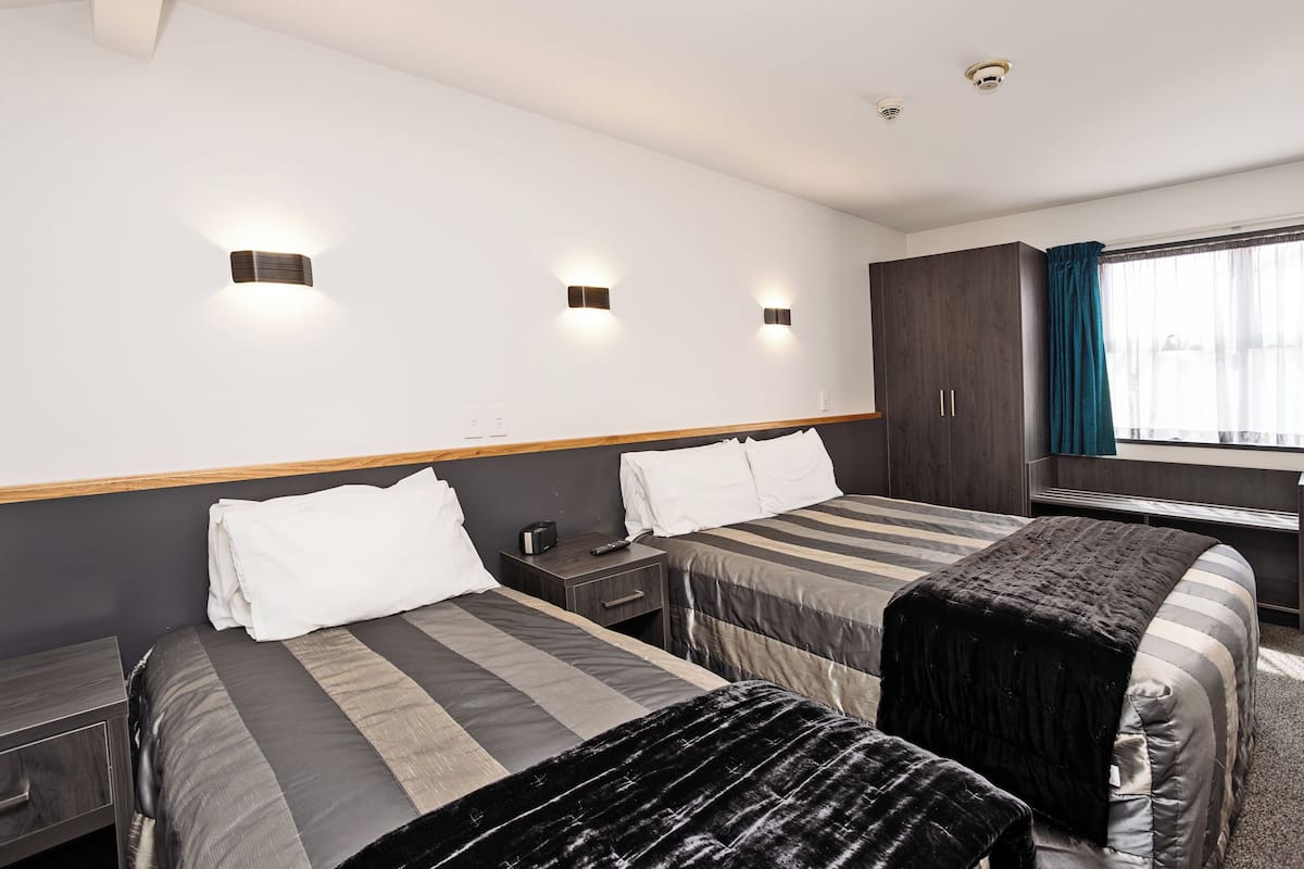 A hotel room with two beds, a desk, a wardrobe, and a window with curtains.
