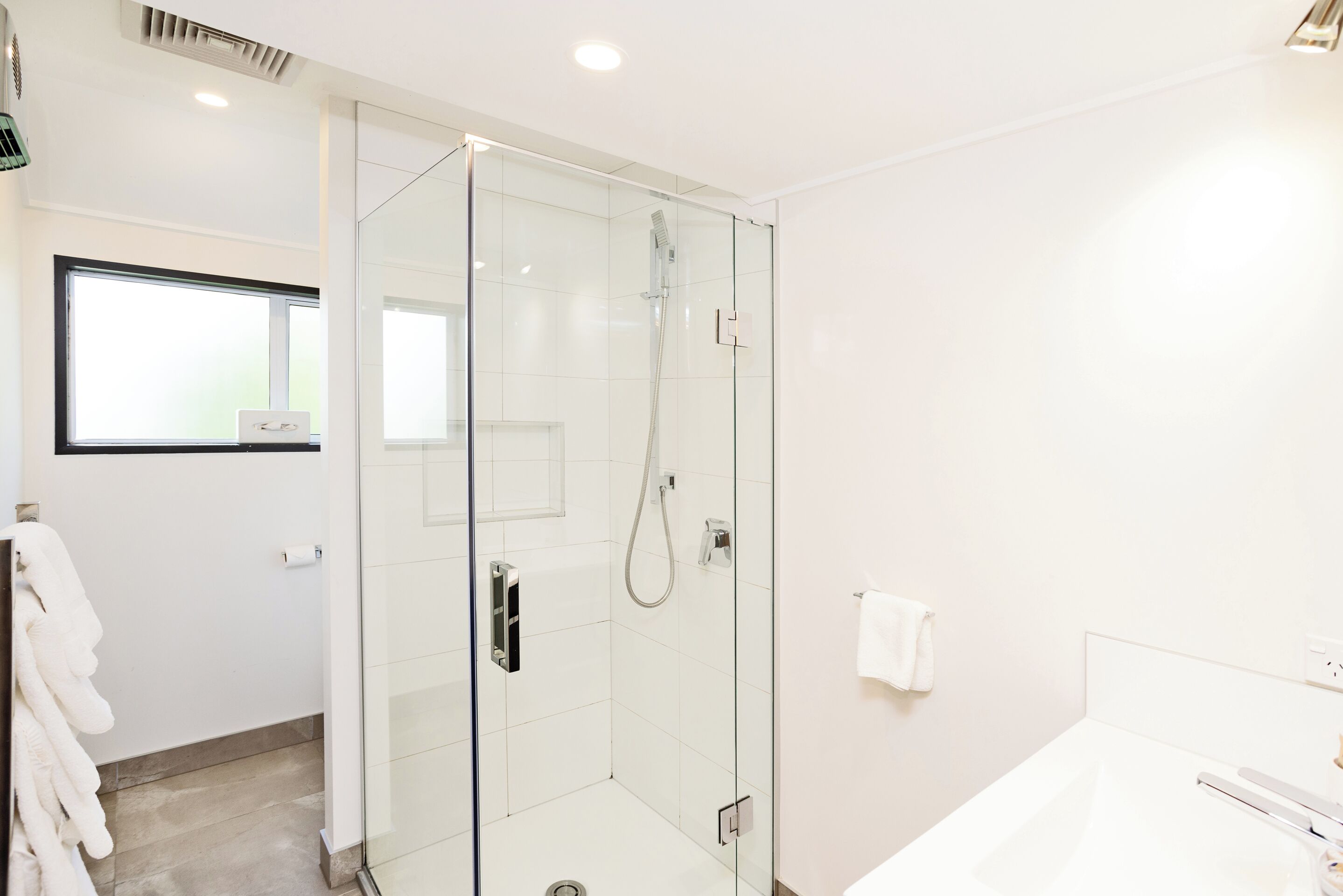 A modern bathroom with a glass-enclosed shower, a white bathtub, and a visible towel rack.