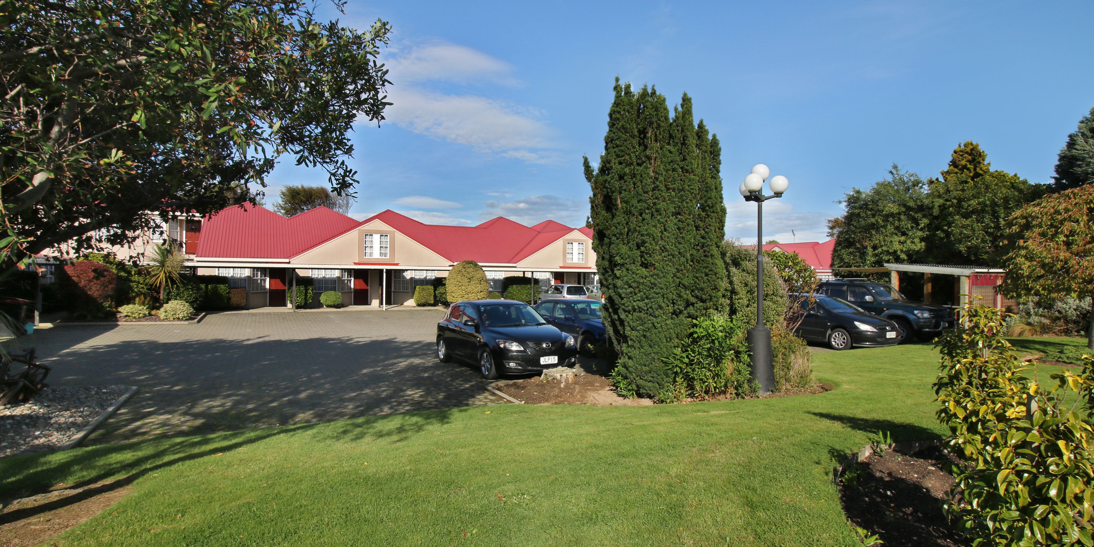 A building with a red roof, parked cars, and a well-maintained lawn.