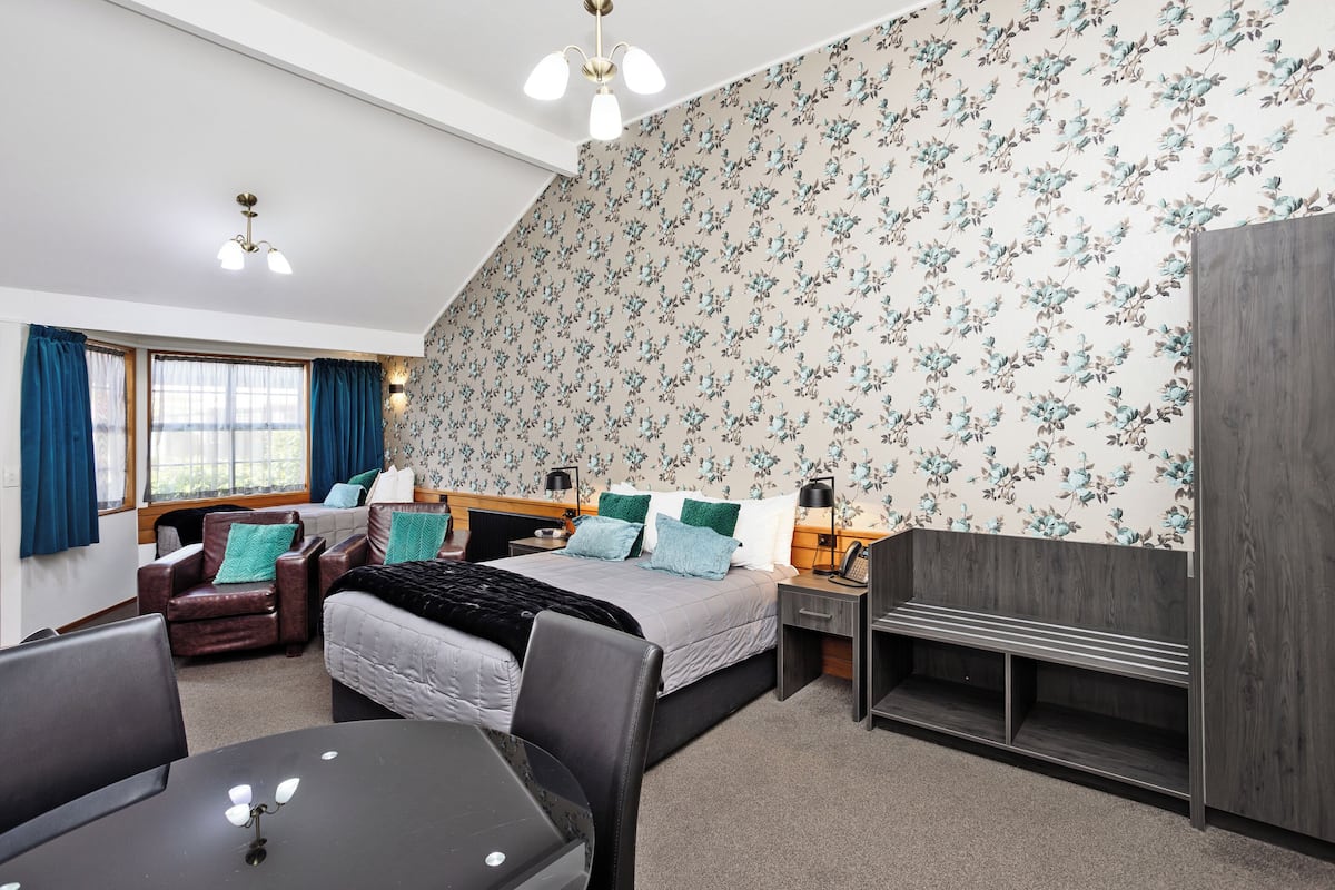 A bedroom with a bed, a desk, a chair, a wardrobe, and a window with curtains.