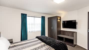 Une chambre d’hôtel avec un lit, un téléviseur fixé au mur, une armoire et une fenêtre avec des rideaux.