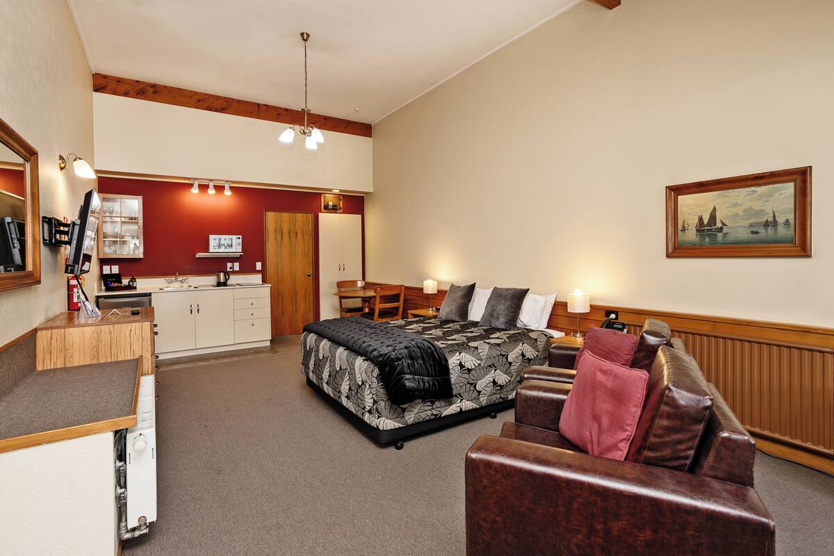 A hotel room with a bed, a sofa, a desk, and a kitchenette.