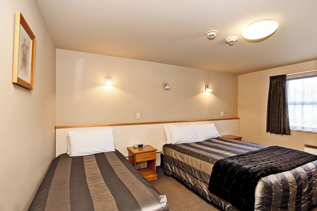A hotel room with two single beds, a nightstand with a lamp, and a window with curtains.