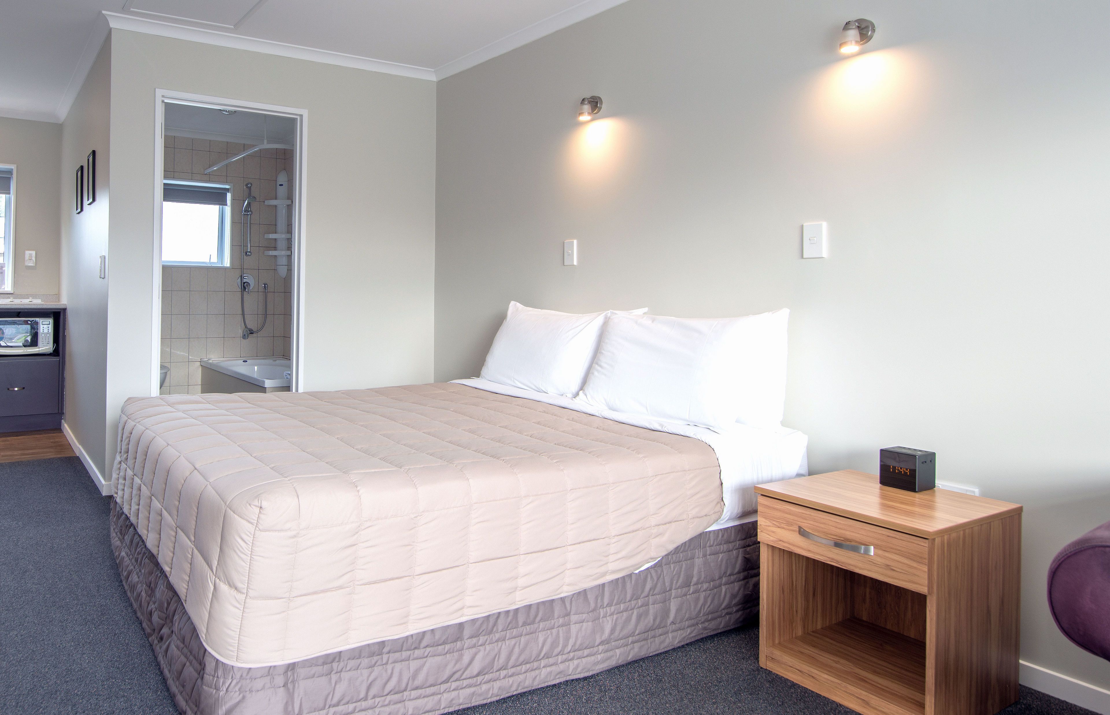 Een slaapkamer met een bed, een houten nachtkastje, een wandlamp en een douche.