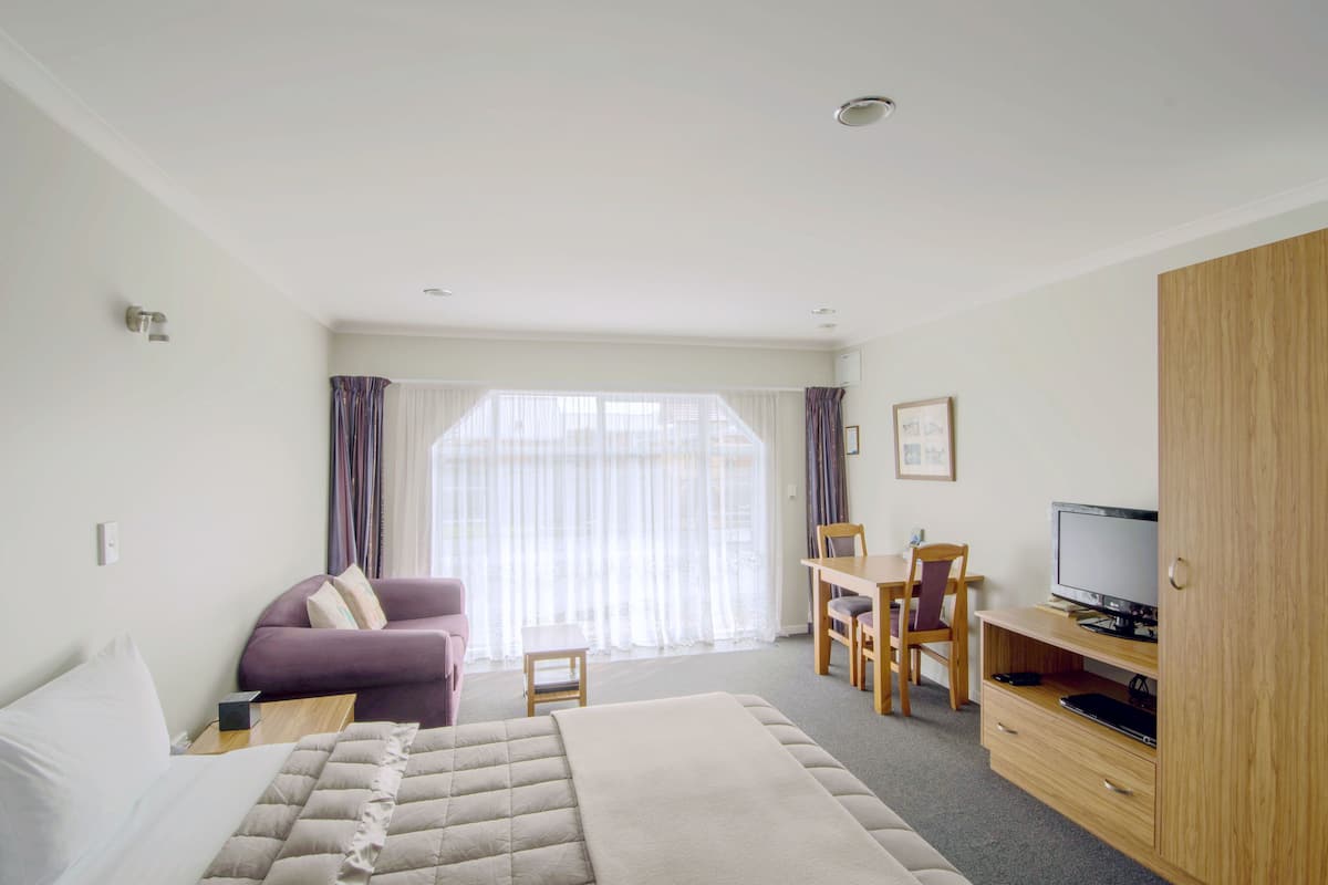 A hotel room with a bed, a sofa, a desk with a chair, a television, and a wardrobe.