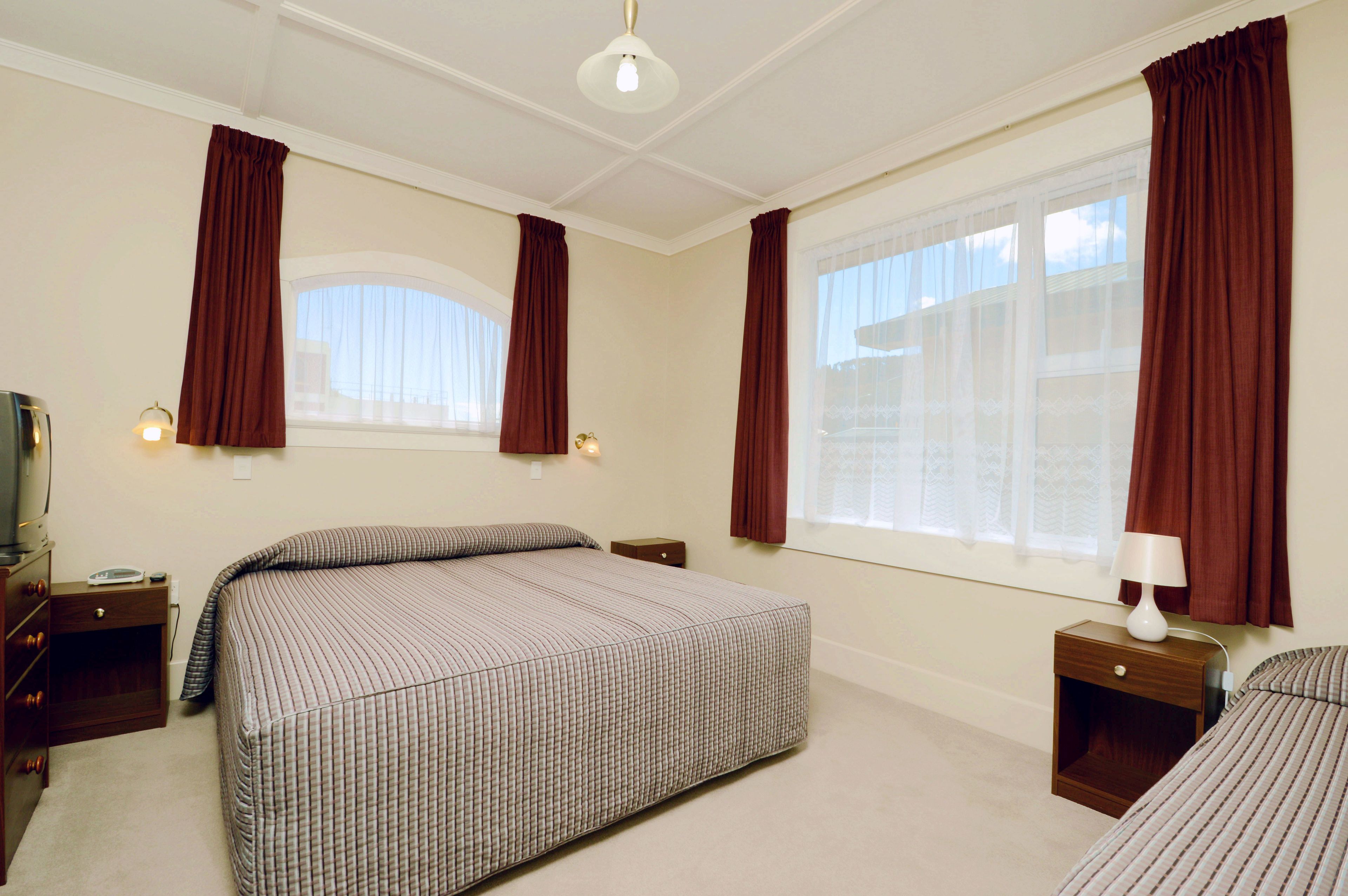 Un dormitorio con una cama grande, dos mesitas de noche, una lámpara y una ventana con cortinas.