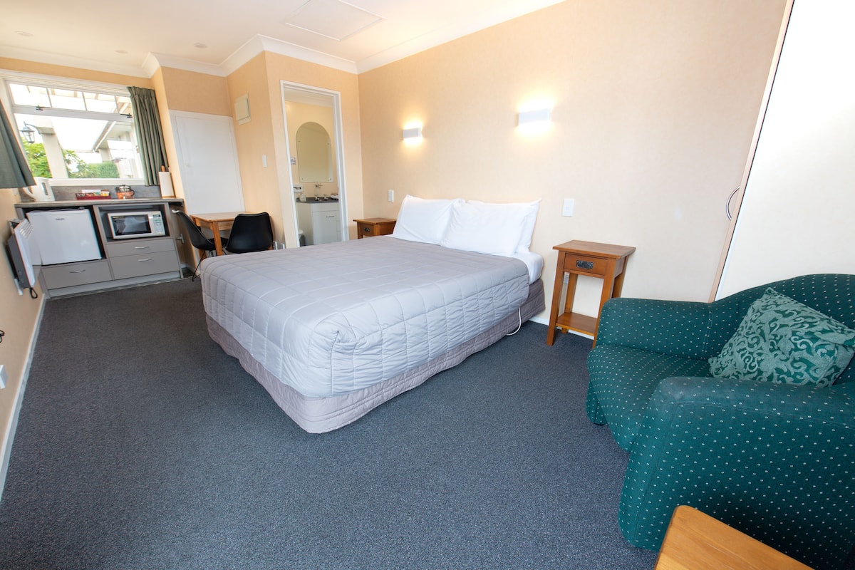 A hotel room with a bed, a green sofa, a desk with a microwave, and a small kitchenette.