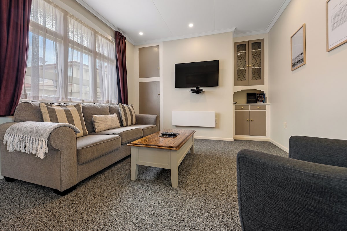 A living room with a sofa, a coffee table, and a TV mounted on the wall.