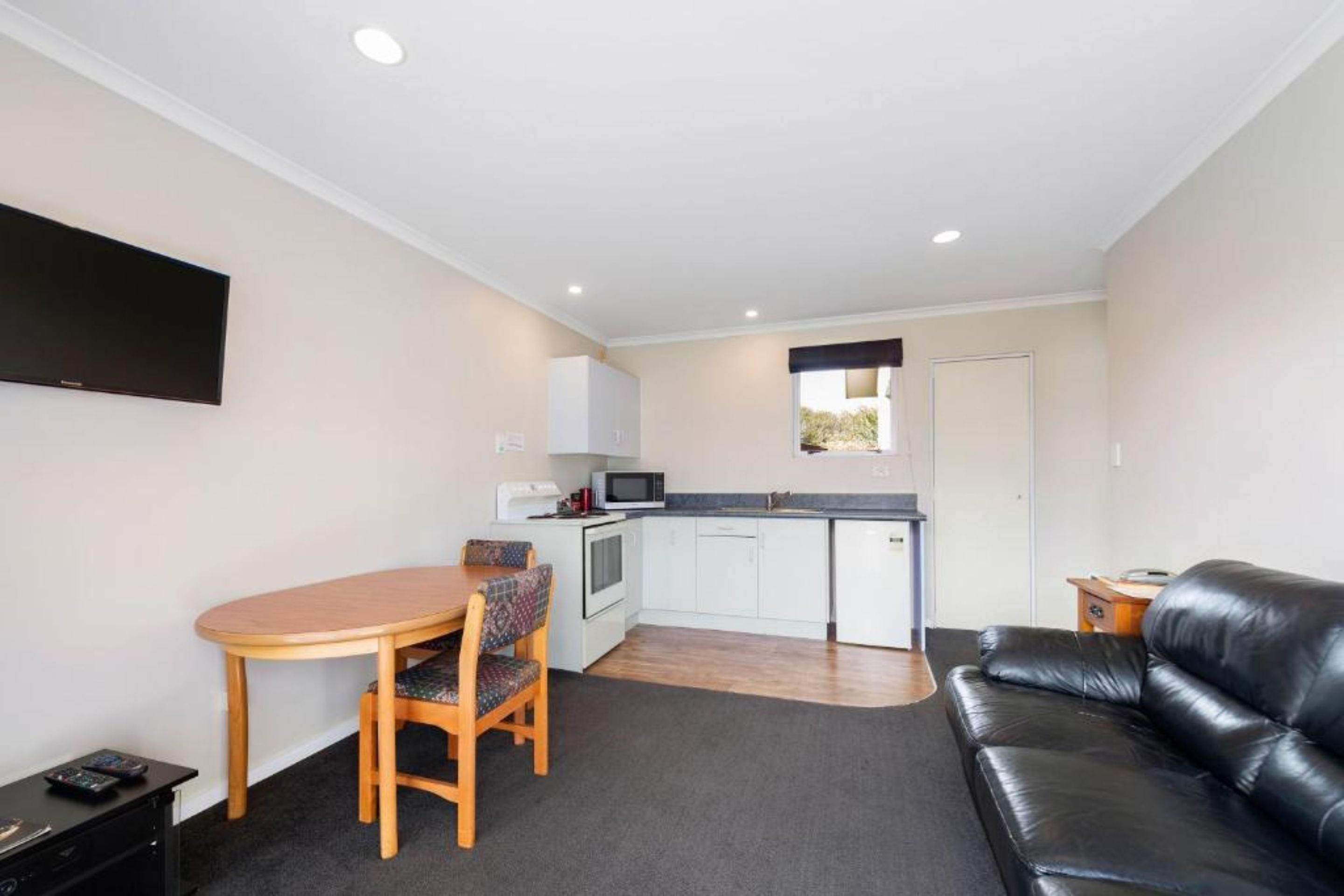 A compact living space with a dining area, kitchenette, and a black leather sofa.