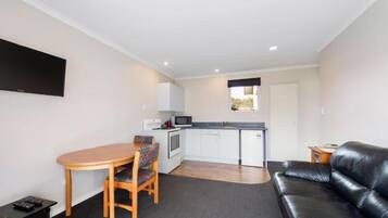 A compact living space with a dining area, kitchenette, and a black leather sofa.
