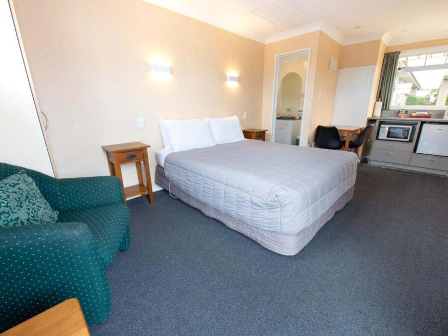 Habitación de hotel con cama, sofá verde, una mesita, escritorio con computadora y kitchenette.
