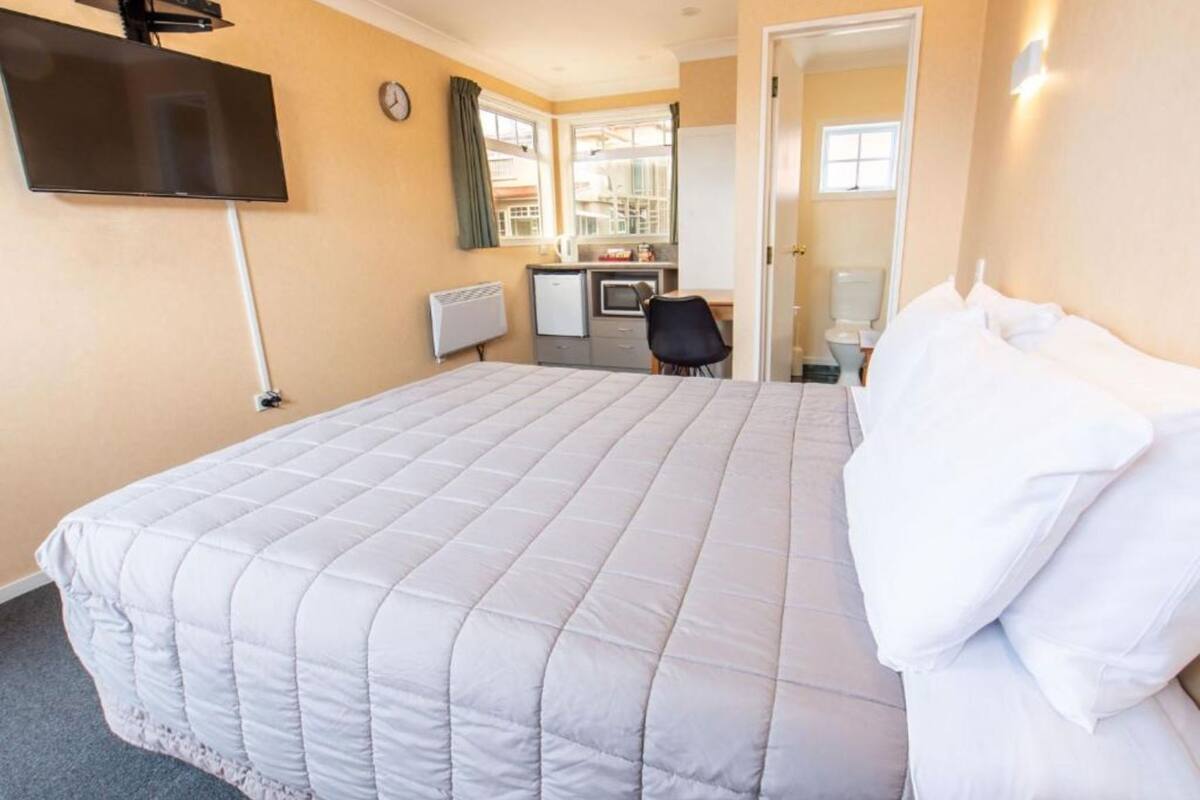 A hotel room with a bed, a desk, a chair, a TV, and a window.