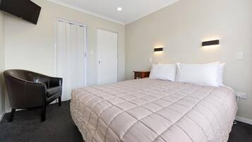 A hotel room with a large bed, a chair, two doors, and a flat-screen TV mounted on the wall.
