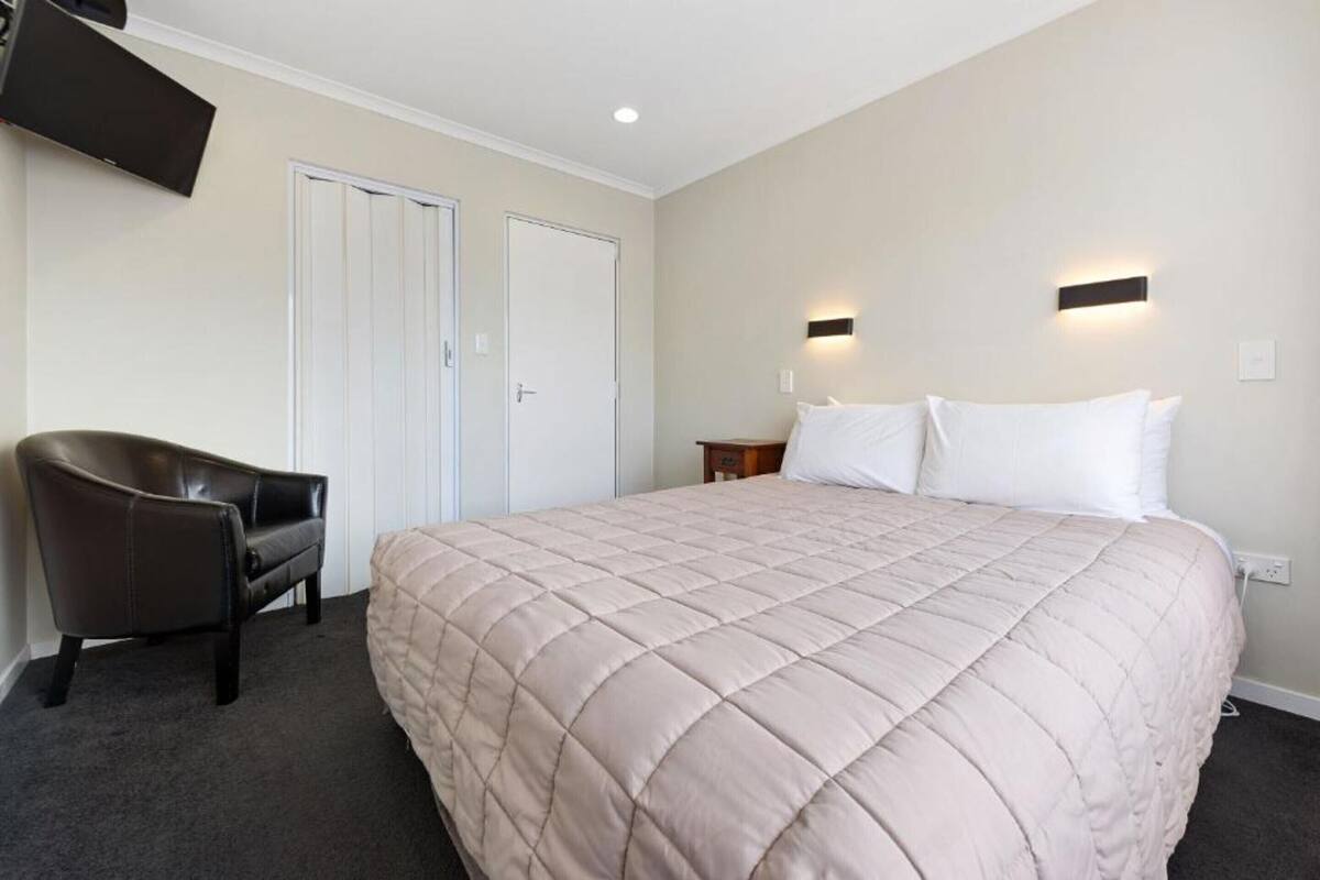 A hotel room with a bed, a chair, a TV mounted on the wall, and two doors.