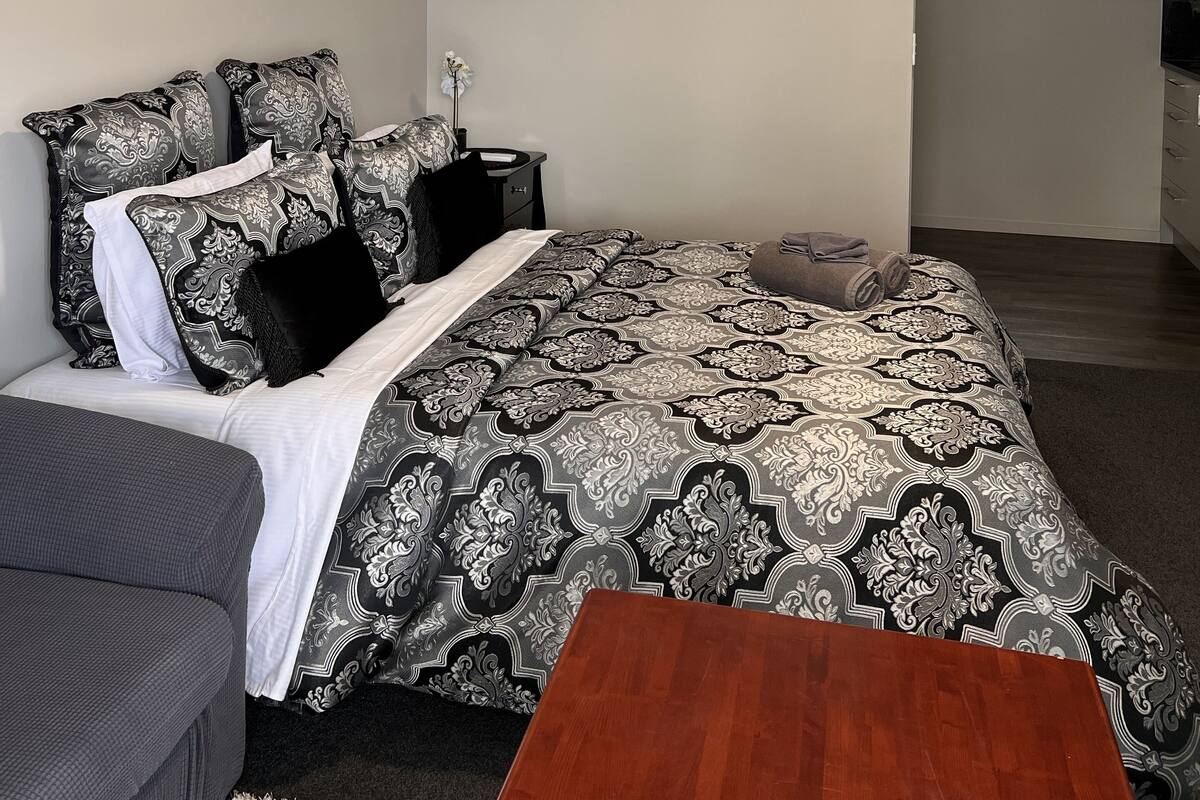 Um quarto com cama, mesa de cabeceira, cômoda, mesa de madeira e janela.