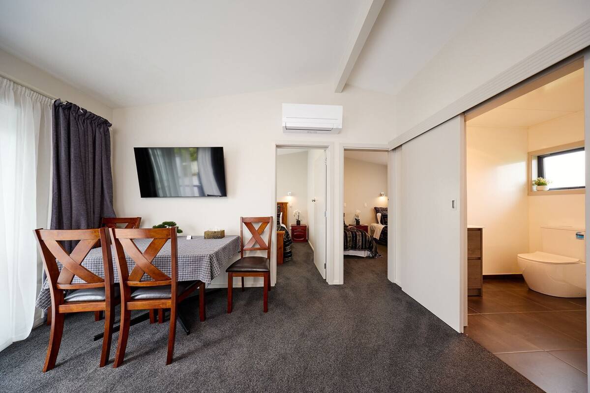 Quarto de hotel moderno com área de refeições, TV, ar-condicionado e banheiro.