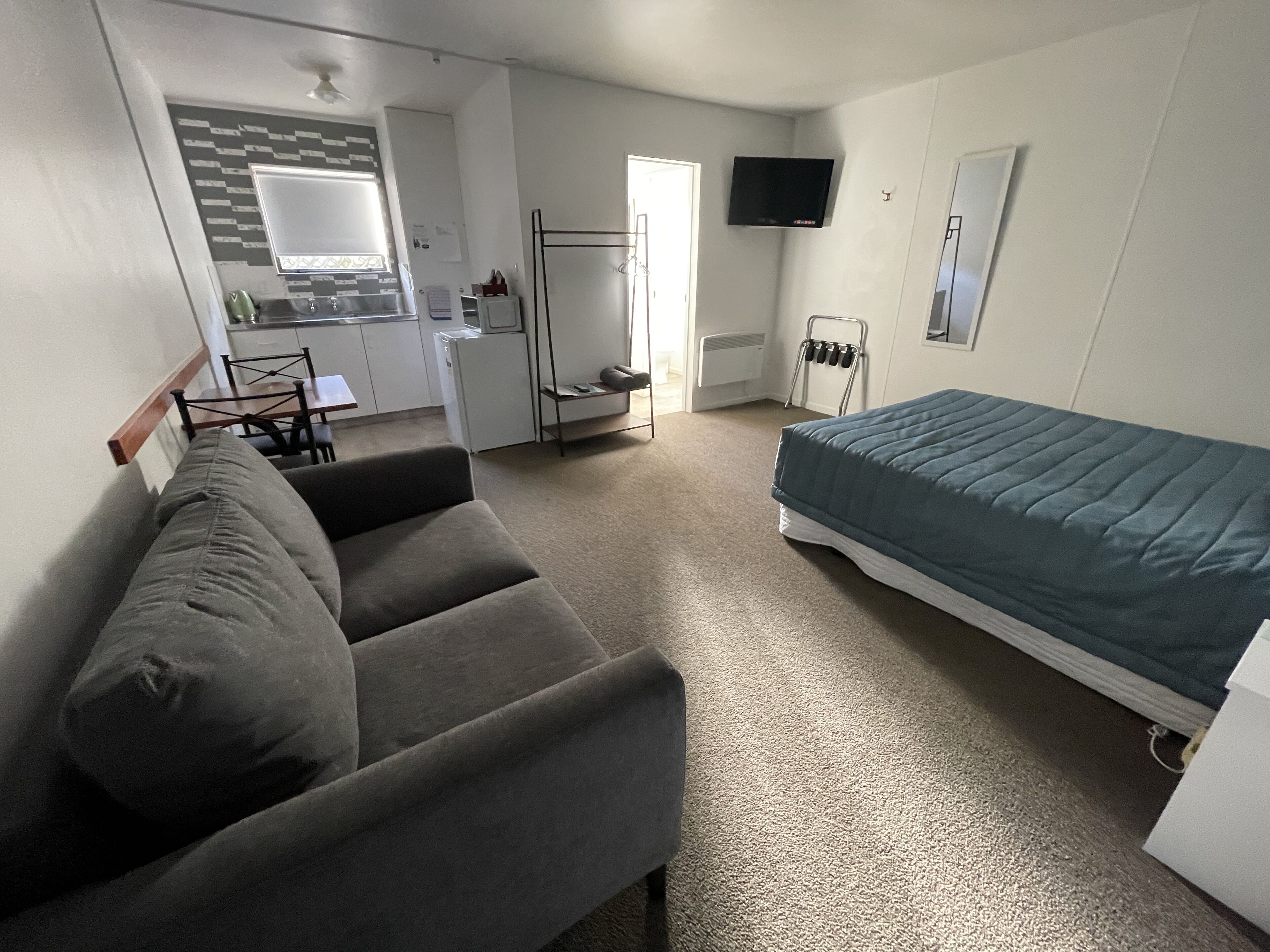 A compact room with a sofa, a bed, a TV, and a kitchenette.