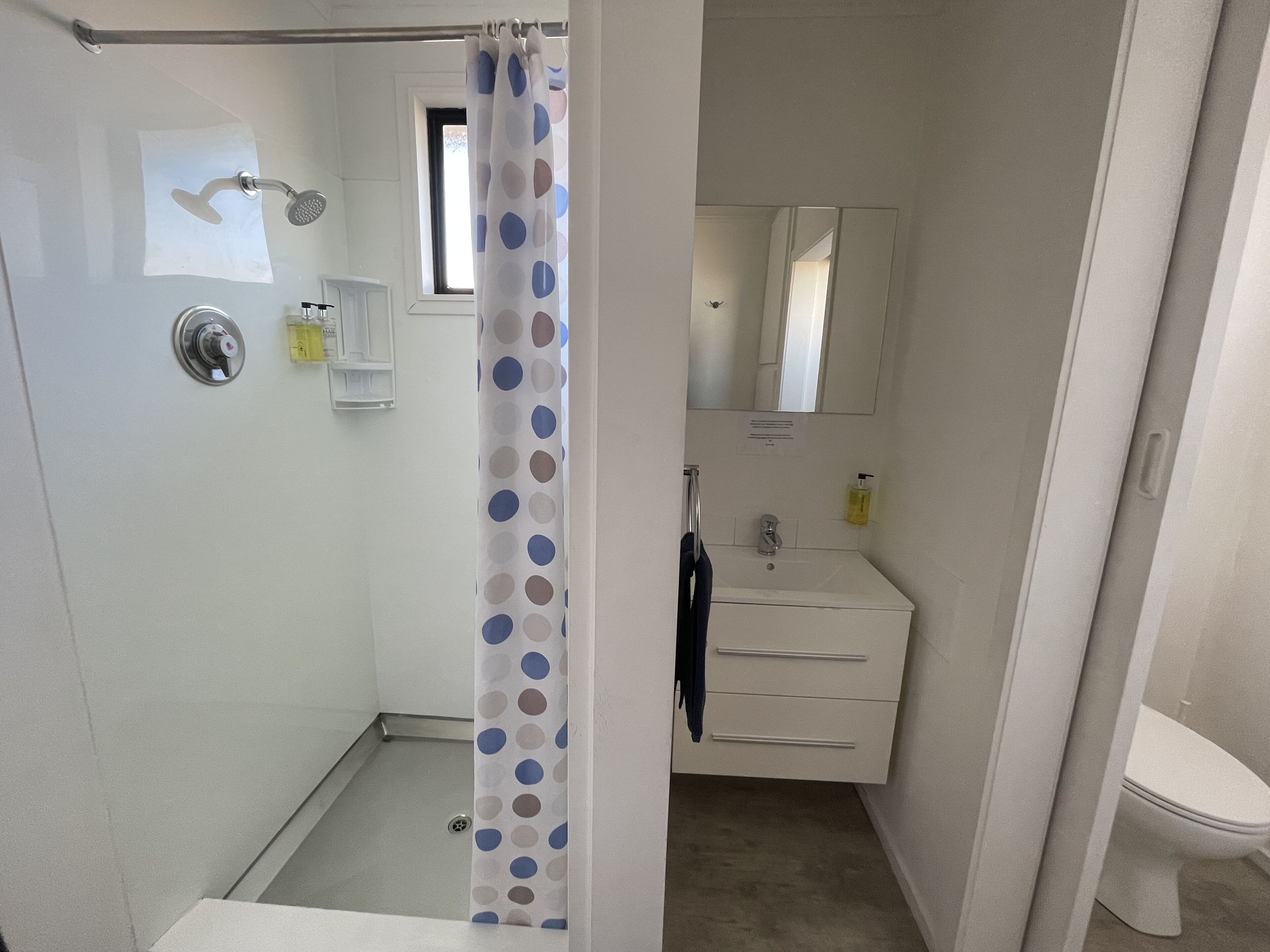 Un baño con ducha, lavamanos con espejo e inodoro.