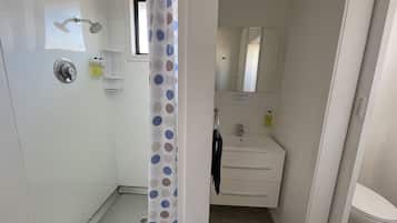 Un baño con ducha, lavamanos con espejo e inodoro.