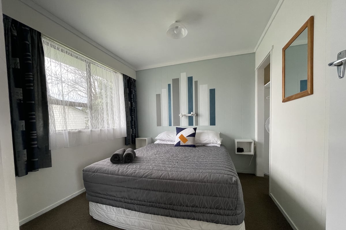 Um quarto com uma cama, mesa de cabeceira, espelho e janela com cortinas.