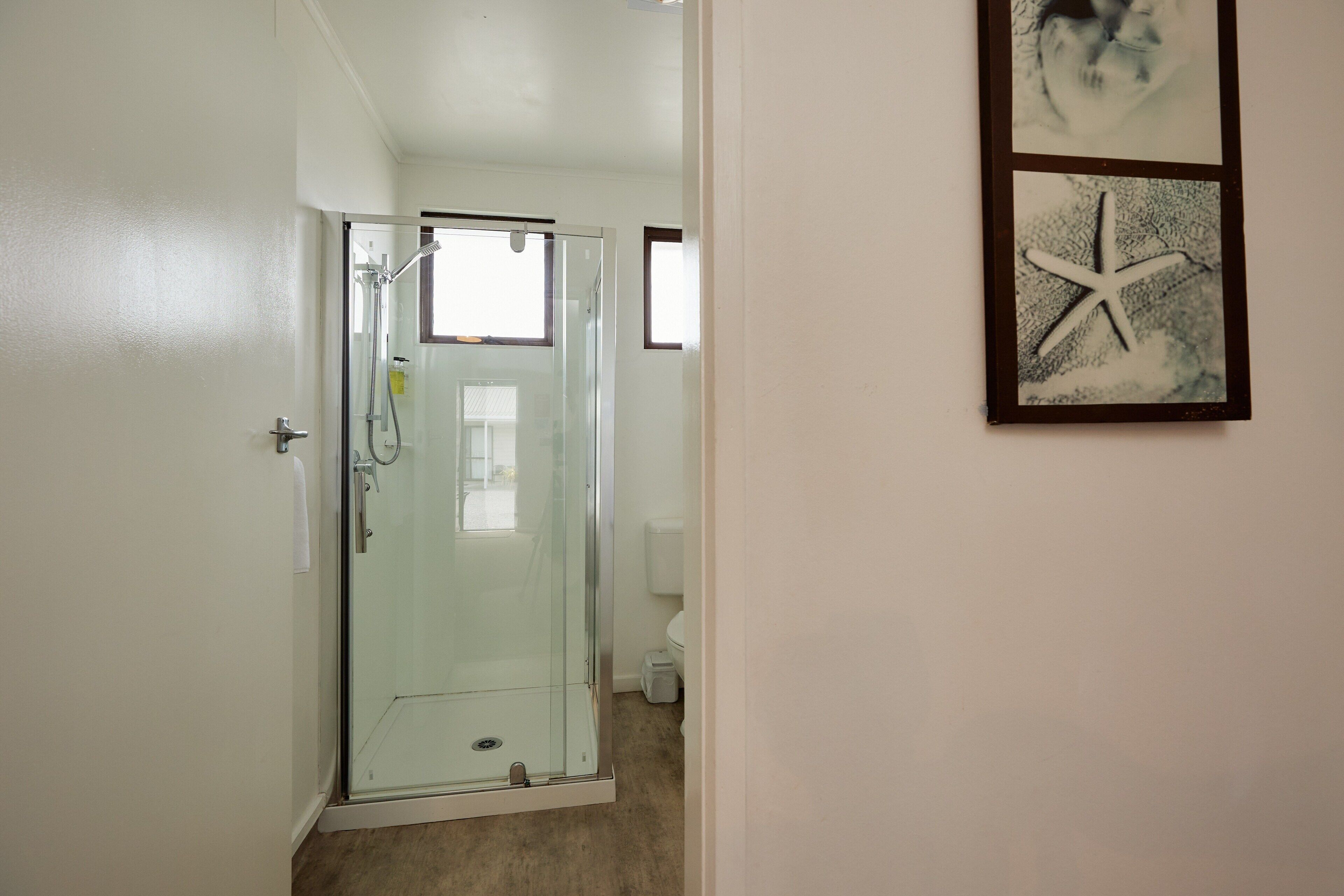 Ein Duschraum mit Glastüren und einem sichtbaren WC im Hintergrund.
