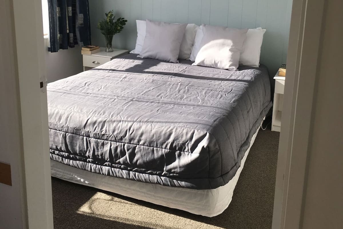 Um quarto com cama, mesa de cabeceira, luminária e janela com cortinas.