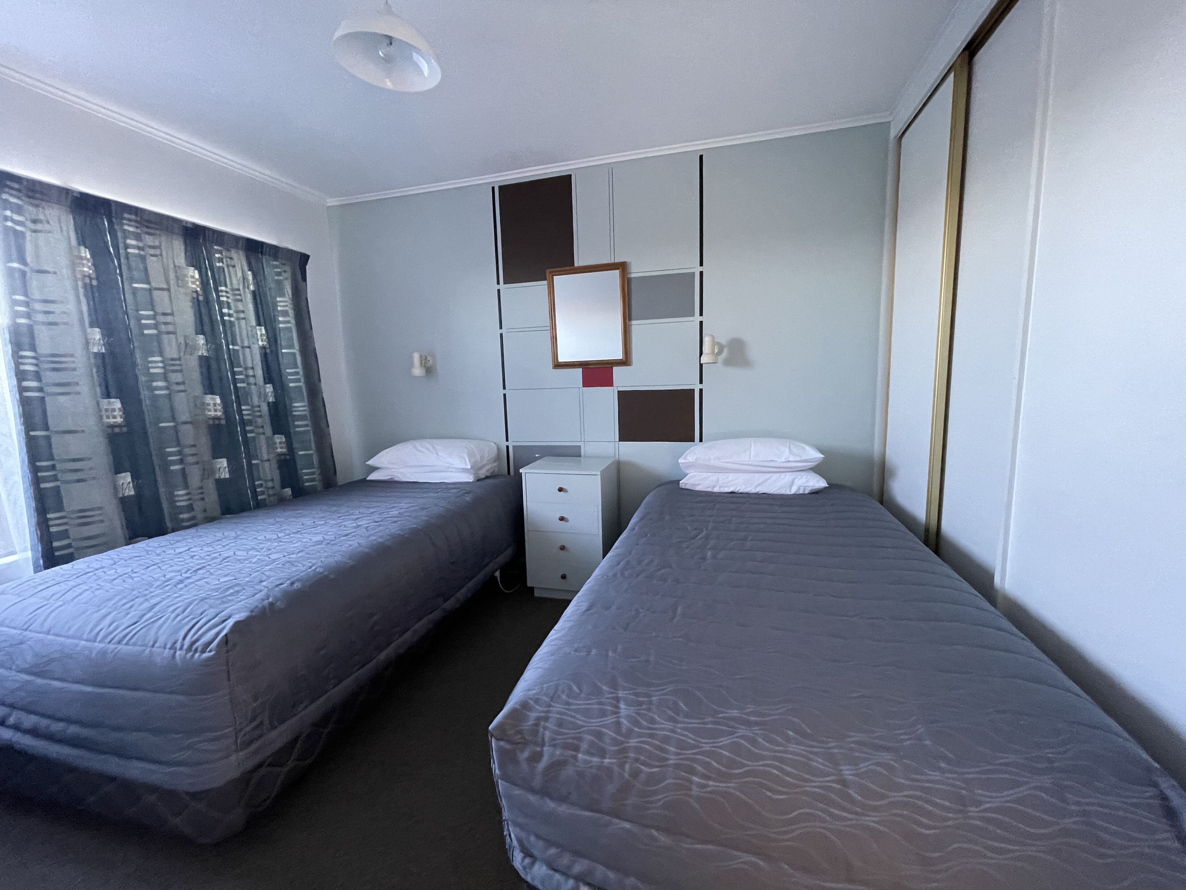 A hotel room with two single beds, a dresser, a mirror, and a window with curtains.