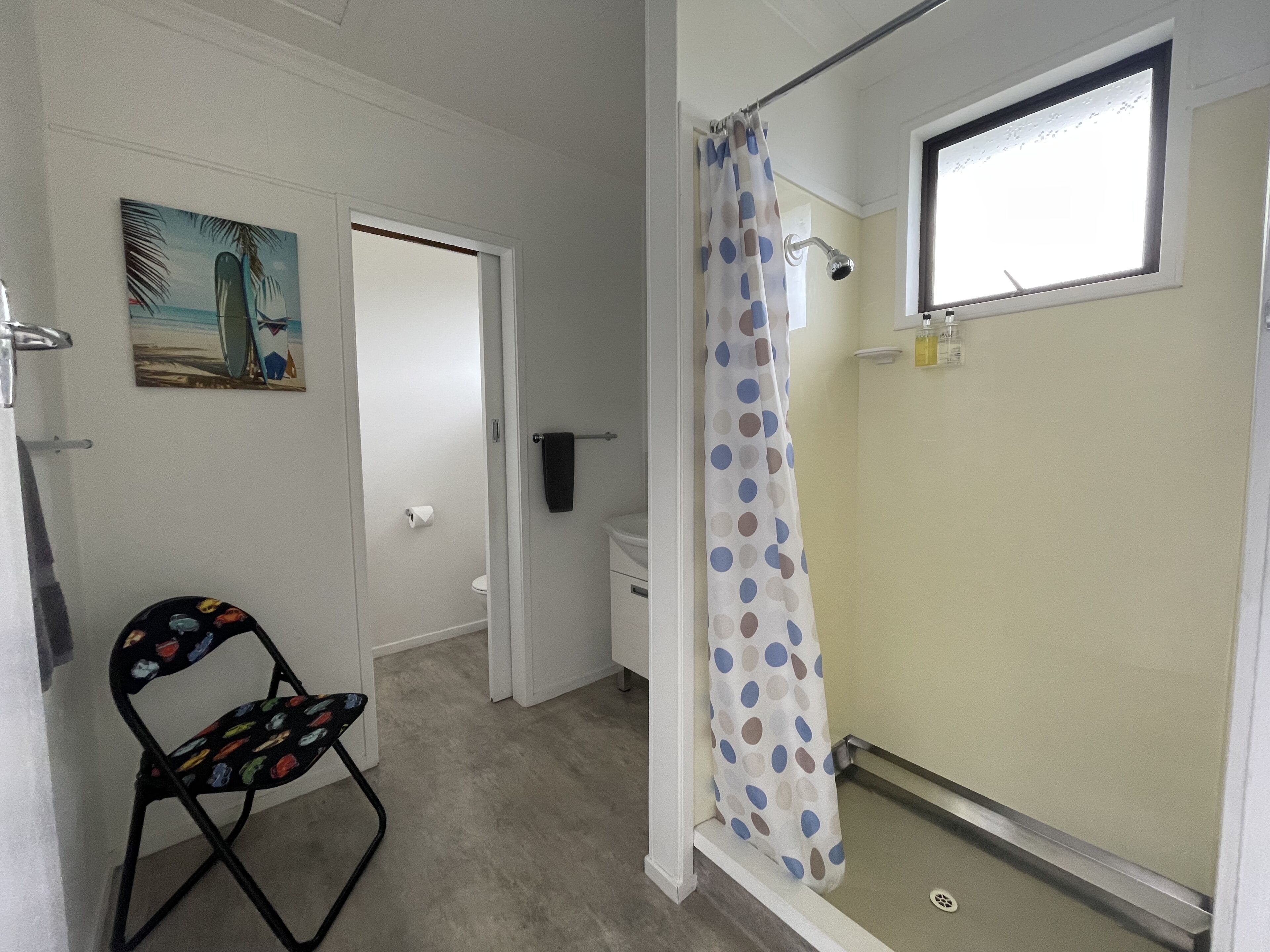 A bathroom with a shower, toilet, and a chair.