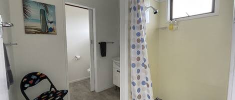 A bathroom with a shower, toilet, and a chair.