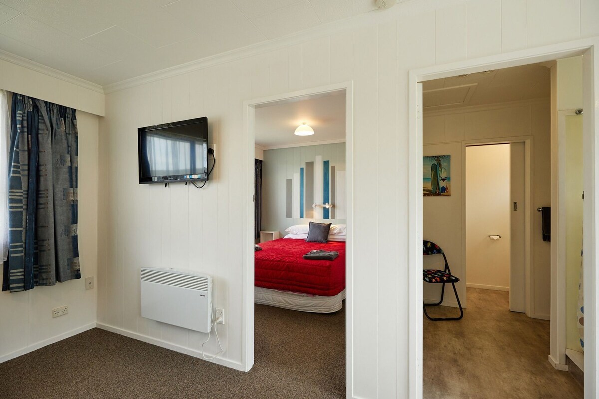A hotel room with a bed, a TV mounted on the wall, a radiator, and a door leading to another room.