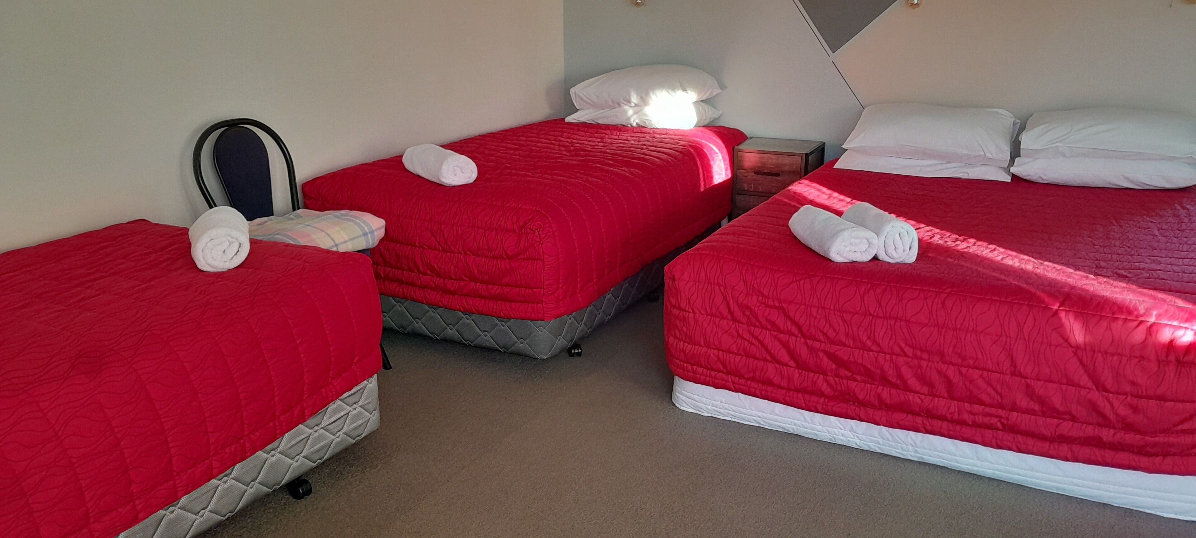 A hotel room with three single beds, each with a red bedspread and white pillows.