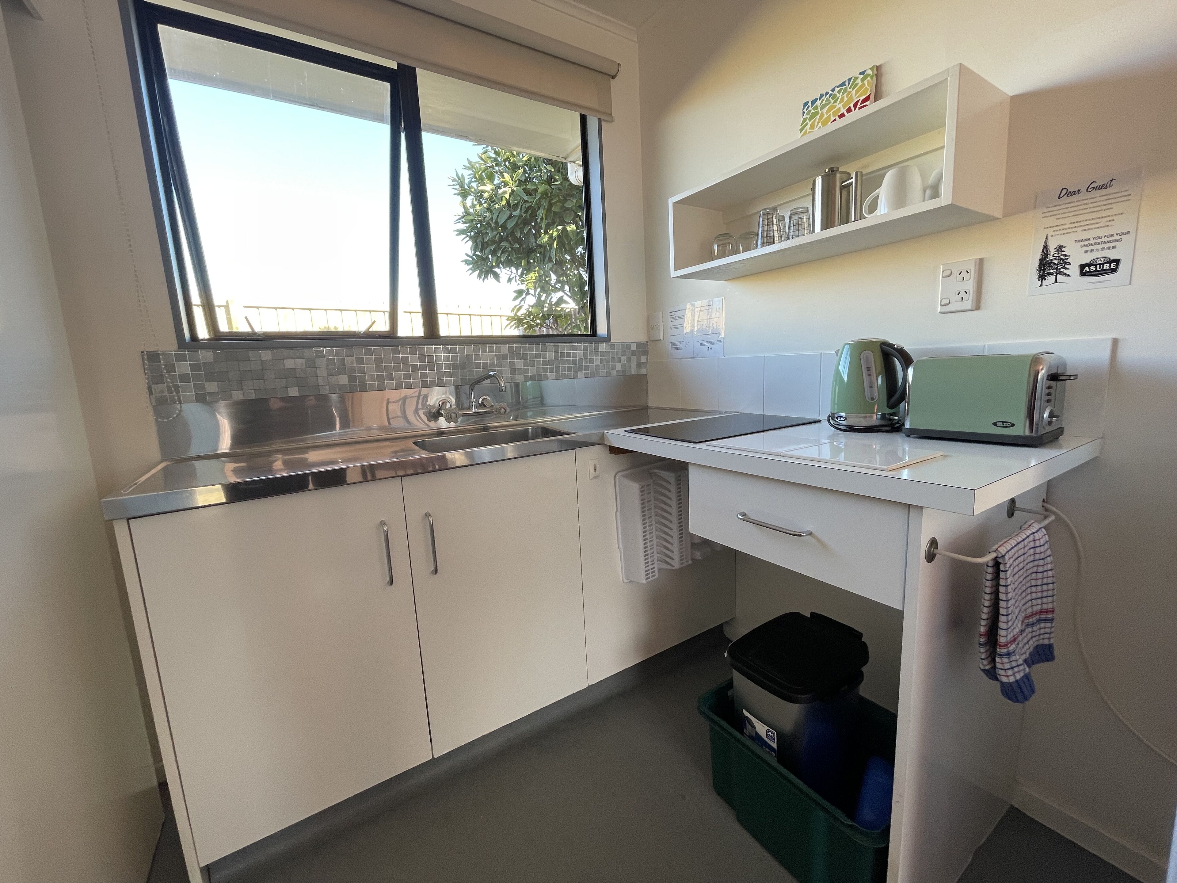 Een moderne keuken met een roestvrijstalen spoelbak, een groene toaster en een raam met uitzicht op bomen.