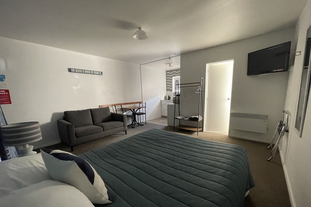 Quarto com cama, sofá, escrivaninha e televisão.