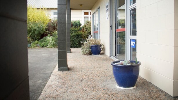 A building entrance with a covered porch, large potted plants, and a sign indicating a Sky lounge.