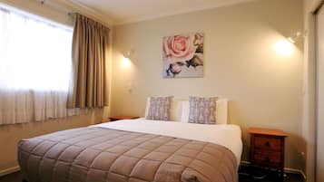 A bedroom with a bed, two nightstands, a wall-mounted light, a window with curtains, and a framed picture on the wall.