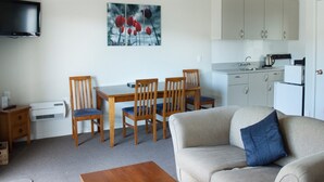 A living room with a sofa and a dining table with chairs. There is a kitchen area with cabinets and a microwave. A flat-screen TV is mounted on the wall.