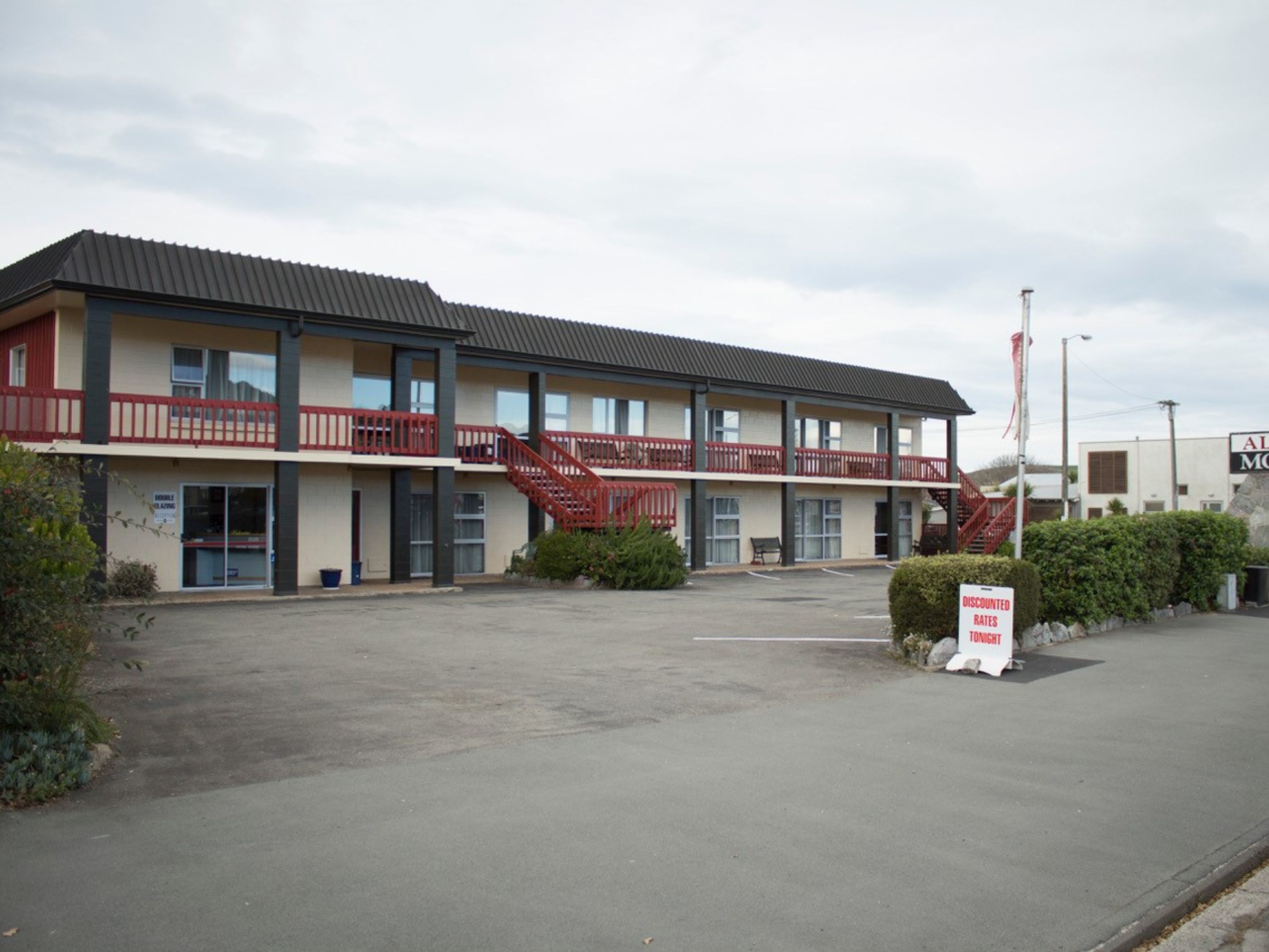 Un motel de dos pisos con un balcón rojo y un letrero que indica tarifas reducidas.