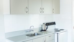 A kitchen with white cabinets, a stainless steel sink, a kettle, and a stove.