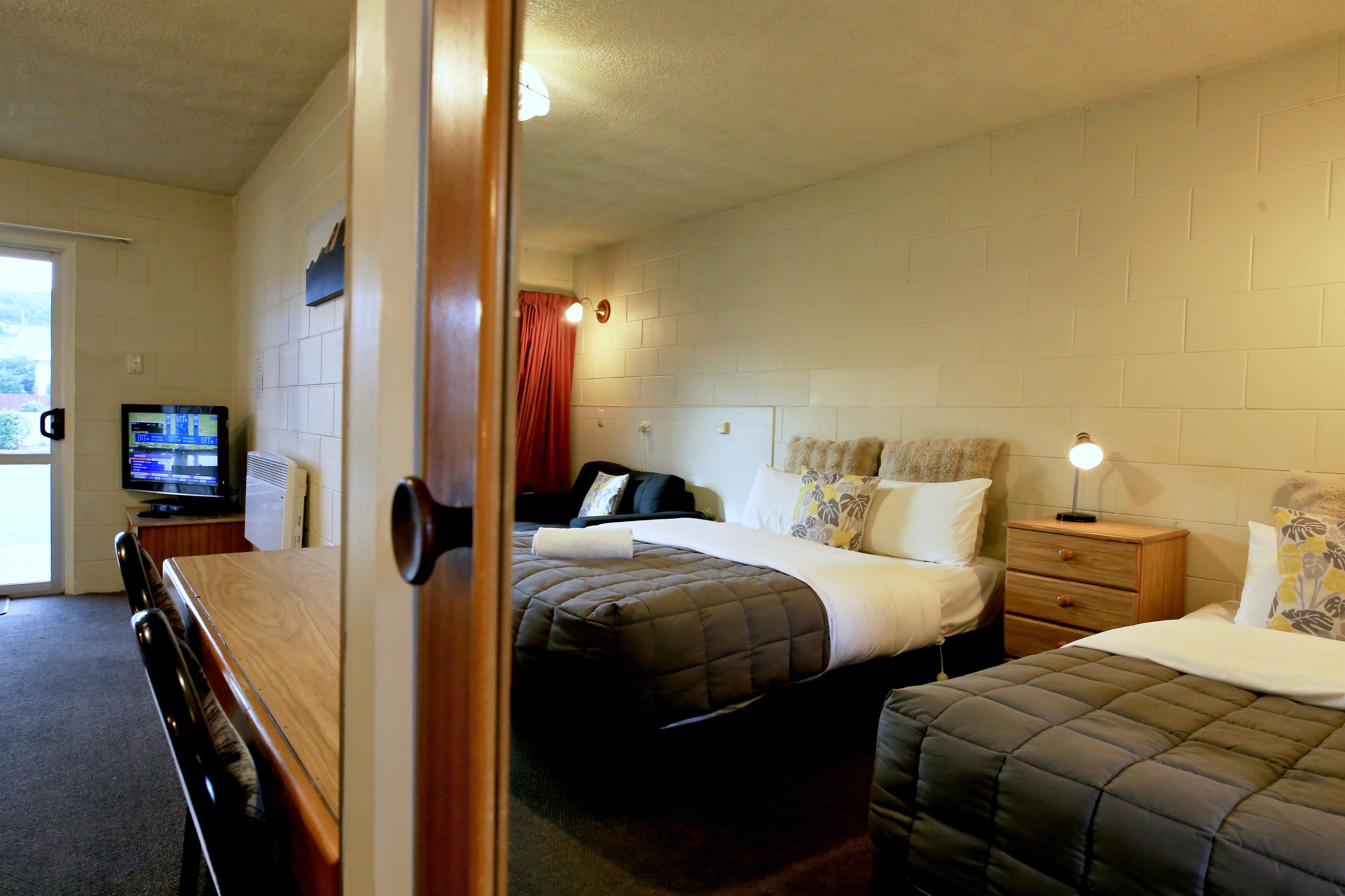 Une chambre d’hôtel avec un lit, une table de chevet, une lampe et un téléviseur posé sur un meuble.