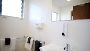 A bathroom with a white sink, a mirror, a towel rack with towels, and a hand dryer.