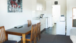 A compact kitchen with white cabinets, a dining table with chairs, and a refrigerator.